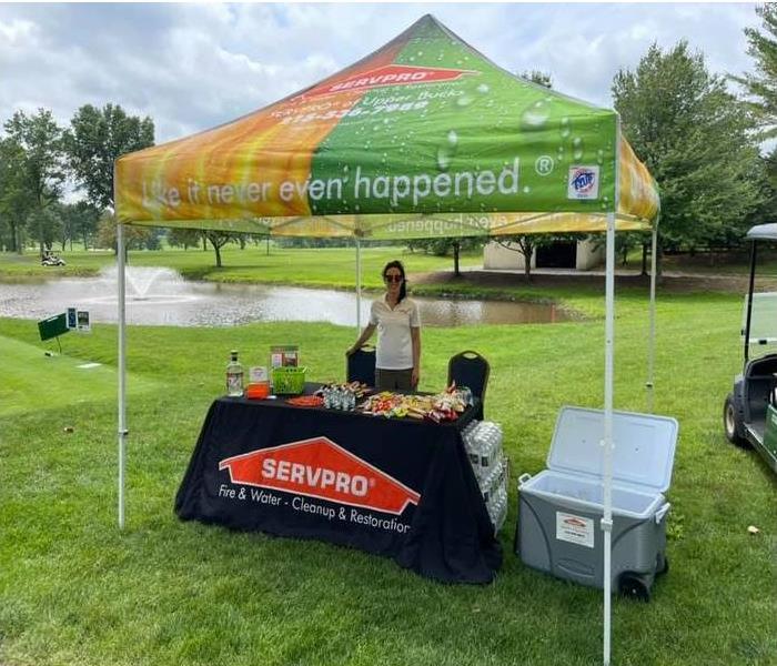 a woman standing behind a SERVPRO table with a tent overhead