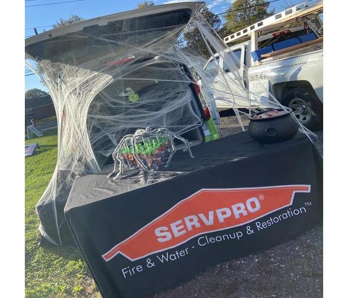 Car trunk is covered in decor spiderwebs, a SERVPRO table sits in front with cups and a cauldron